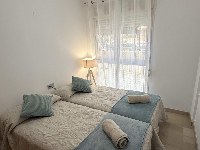 Dormitorio secundario con dos camas individuales y armario, ideal para familias en el apartamento de Denia