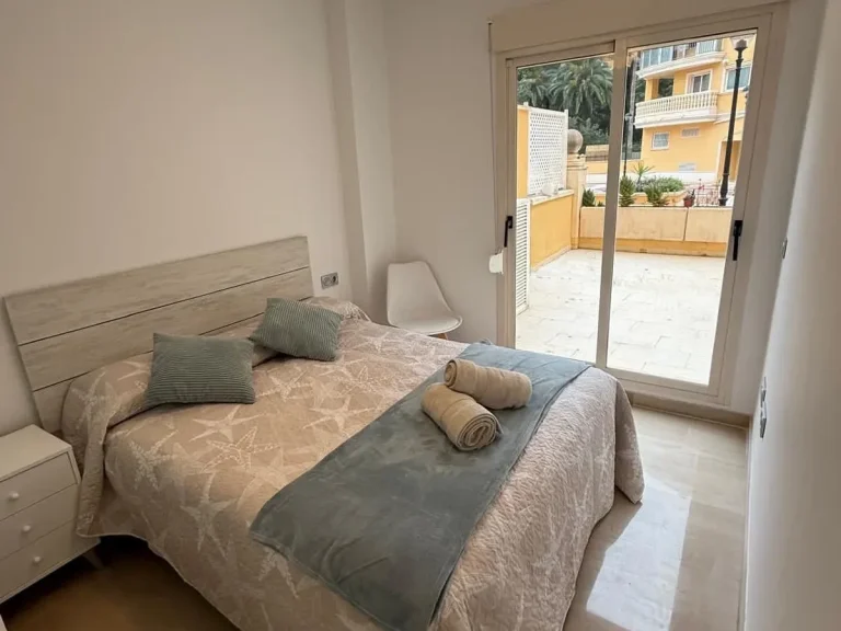 Dormitorio principal con cama de matrimonio, armario empotrado y ventana con vistas a los jardines de la urbanización en Denia