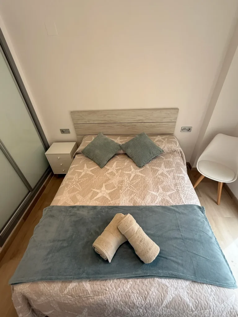 Dormitorio principal con cama de matrimonio, armario empotrado y ventana con vistas a los jardines de la urbanización en Denia