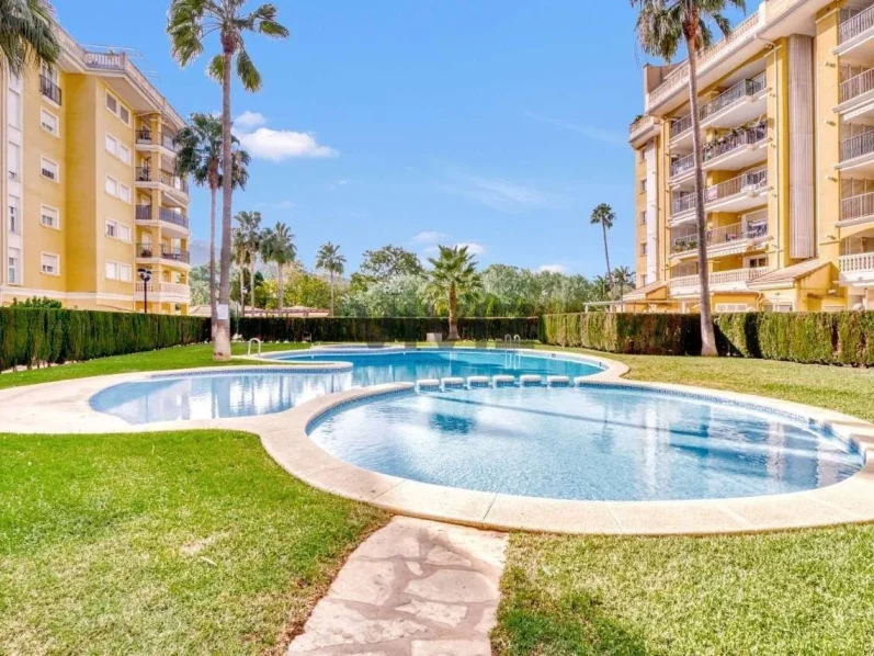 Piscina comunitaria en la urbanización del apartamento, rodeada de jardines y césped, ideal para disfrutar del sol en Denia